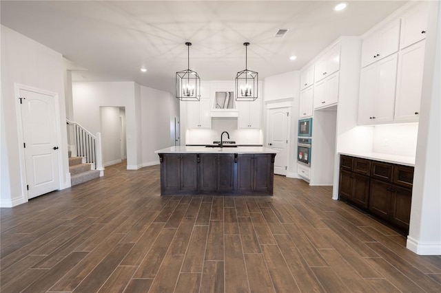 kitchen featuring pendant lighting, built in microwave, an island with sink, stainless steel oven, and dark wood-type flooring