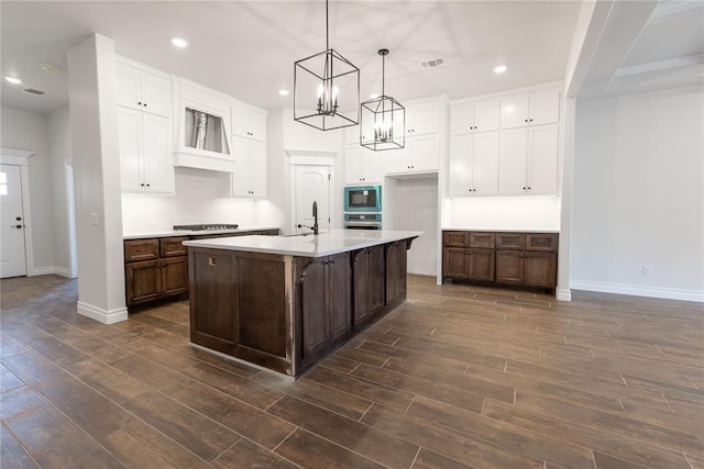 kitchen featuring gas cooktop, hanging light fixtures, dark brown cabinets, an island with sink, and dark hardwood / wood-style flooring