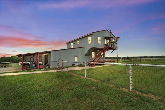 back of house at dusk featuring an outbuilding, a rural view, a yard, and fence