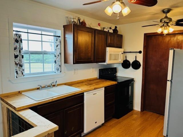 kitchen featuring white appliances, light wood finished floors, butcher block counters, dark brown cabinets, and a sink