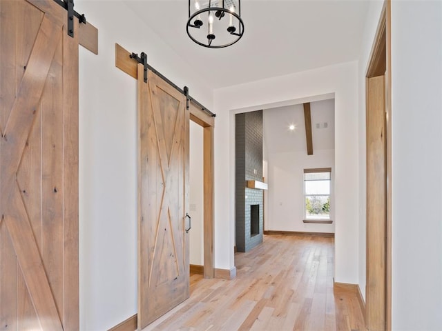 corridor featuring lofted ceiling with beams, light wood finished floors, a barn door, and baseboards