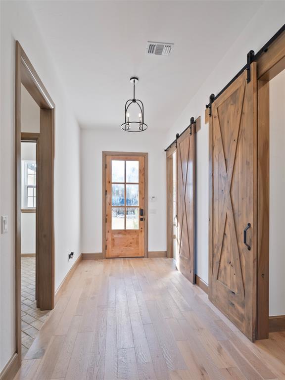 interior space featuring light wood-type flooring, a barn door, visible vents, and baseboards