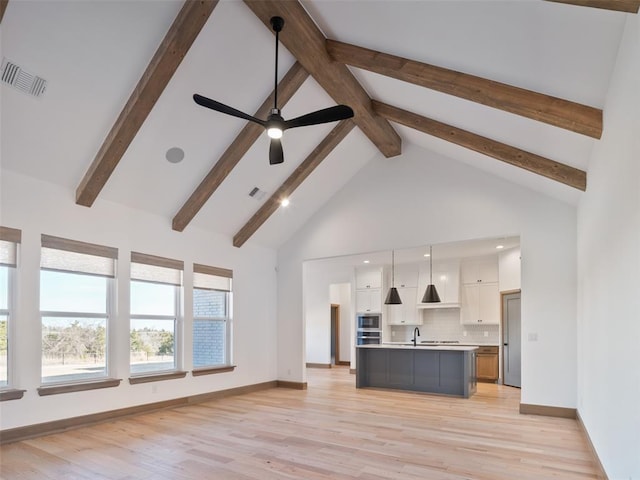kitchen featuring white cabinetry, open floor plan, light countertops, a center island with sink, and pendant lighting