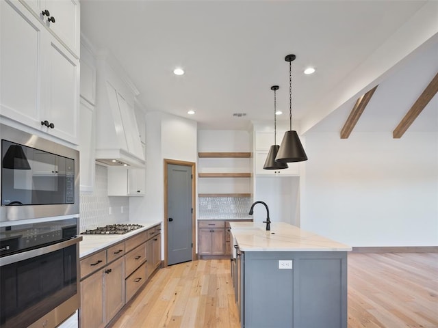 kitchen featuring stainless steel appliances, white cabinets, a center island with sink, and open shelves