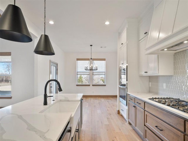 kitchen with white cabinets, custom range hood, hanging light fixtures, light stone countertops, and stainless steel appliances