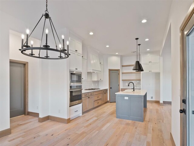 kitchen with a sink, white cabinets, backsplash, a center island with sink, and pendant lighting