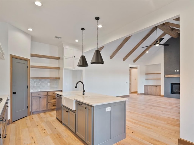 kitchen featuring a kitchen island with sink, a sink, open floor plan, open shelves, and pendant lighting