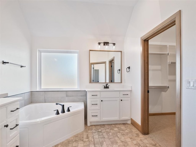 bathroom with a spacious closet, a garden tub, vanity, and baseboards