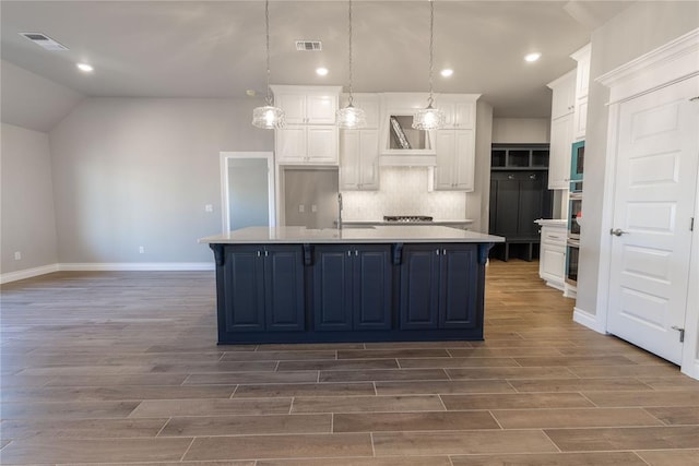 kitchen with pendant lighting, a spacious island, backsplash, blue cabinetry, and white cabinetry