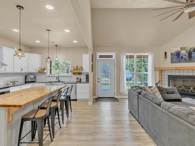 kitchen featuring pendant lighting, white cabinets, stainless steel dishwasher, butcher block countertops, and a kitchen bar