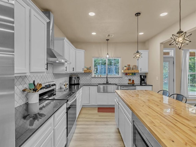 kitchen with pendant lighting, stainless steel electric range, wooden counters, white cabinets, and sink