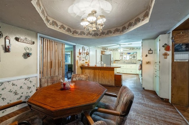 dining space featuring a textured ceiling, ceiling fan with notable chandelier, a tray ceiling, and hardwood / wood-style flooring