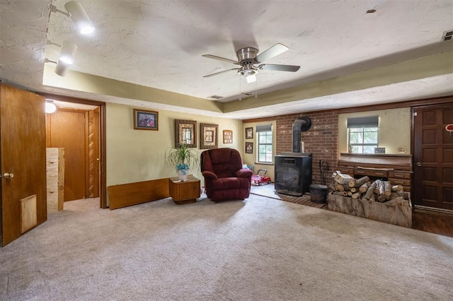 living area with a wood stove, ceiling fan, carpet floors, and a textured ceiling