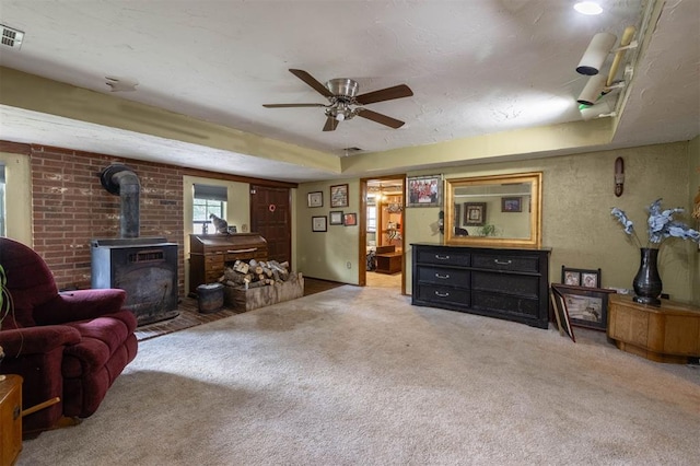 living room featuring carpet flooring, a wood stove, and ceiling fan