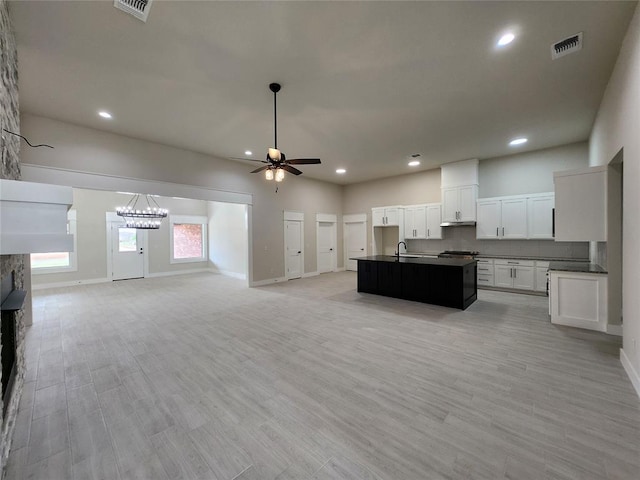 kitchen with ceiling fan with notable chandelier, light hardwood / wood-style flooring, a fireplace, an island with sink, and white cabinetry