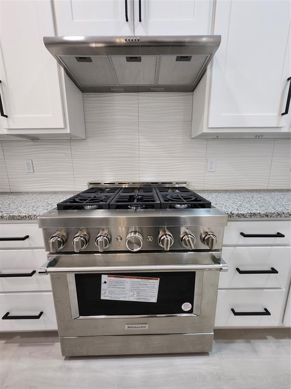 9320 SW 34th St, Oklahoma City, OK 73179 - kitchen featuring high end stainless steel range, decorative backsplash, wall chimney exhaust hood, white cabinetry, and light stone countertops