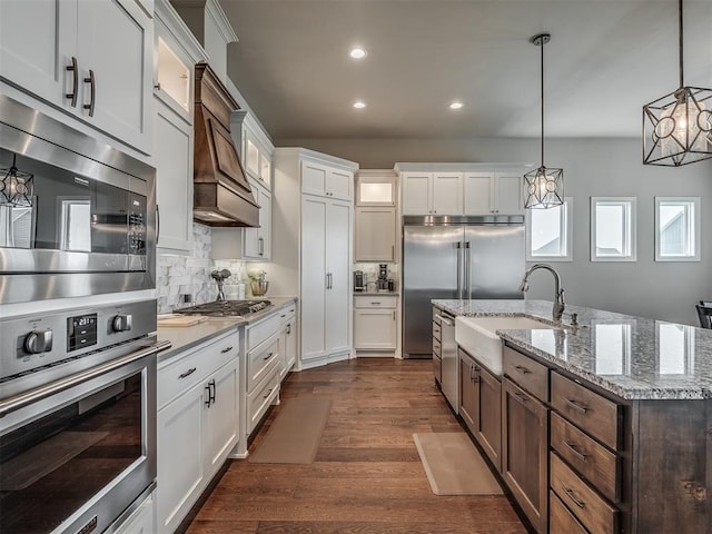 kitchen with sink, white cabinetry, backsplash, built in appliances, and decorative light fixtures