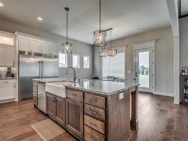 kitchen with sink, hanging light fixtures, stainless steel appliances, a kitchen island with sink, and white cabinets