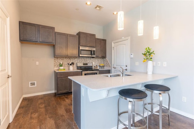 kitchen featuring sink, hanging light fixtures, dark hardwood / wood-style floors, kitchen peninsula, and appliances with stainless steel finishes