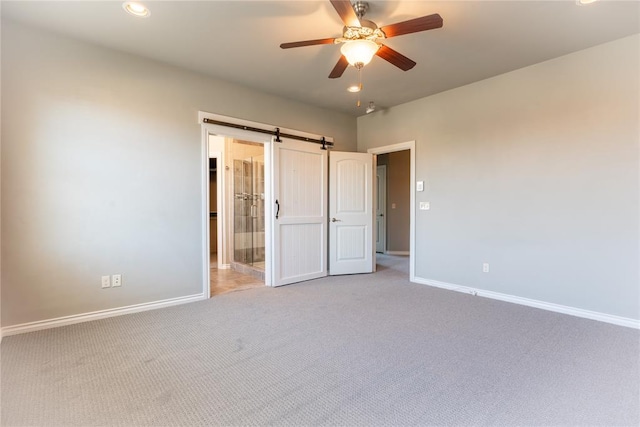 unfurnished bedroom with a barn door, light colored carpet, and ceiling fan