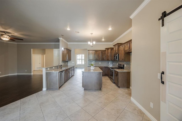 kitchen with a barn door, ornamental molding, appliances with stainless steel finishes, light stone counters, and kitchen peninsula