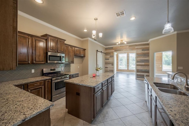 kitchen with crown molding, sink, an island with sink, appliances with stainless steel finishes, and decorative light fixtures