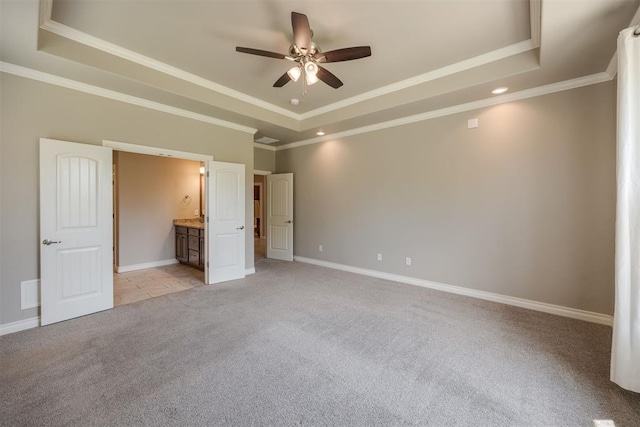 unfurnished bedroom featuring light carpet, ensuite bathroom, a raised ceiling, ceiling fan, and crown molding