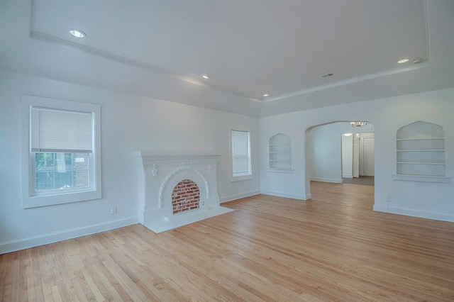 unfurnished living room with built in shelves, light hardwood / wood-style flooring, and a raised ceiling