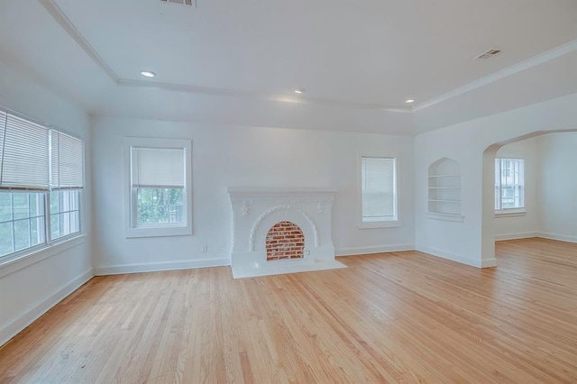 unfurnished living room with built in shelves, ornamental molding, a healthy amount of sunlight, and light wood-type flooring