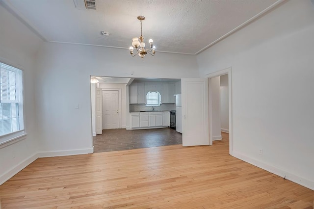 unfurnished living room with light hardwood / wood-style floors, an inviting chandelier, crown molding, and sink