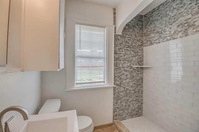 bathroom with toilet, a tile shower, sink, and a wealth of natural light