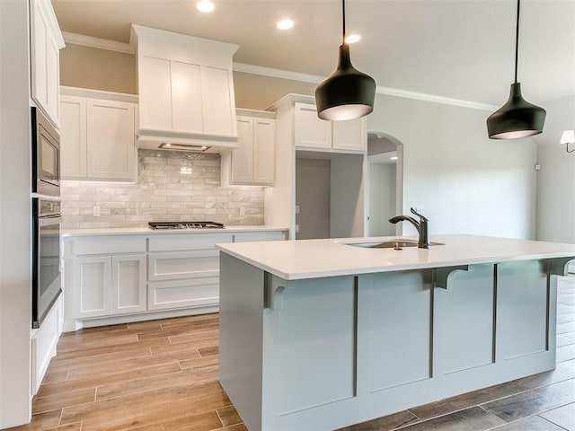 kitchen featuring hanging light fixtures, stainless steel appliances, a kitchen island with sink, white cabinets, and light wood-type flooring