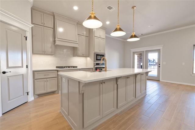 kitchen with gray cabinetry, a kitchen island with sink, crown molding, appliances with stainless steel finishes, and decorative light fixtures