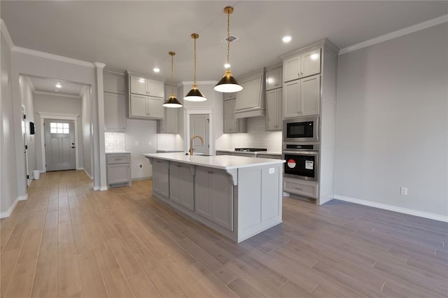 kitchen featuring appliances with stainless steel finishes, gray cabinetry, a kitchen island with sink, pendant lighting, and light hardwood / wood-style floors