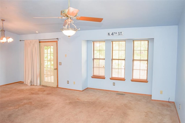 carpeted spare room featuring ceiling fan with notable chandelier