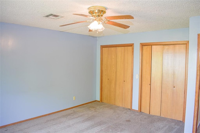 unfurnished bedroom featuring two closets, a textured ceiling, carpet floors, and ceiling fan