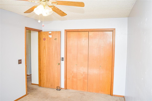 unfurnished bedroom featuring ceiling fan, a textured ceiling, light carpet, and a closet