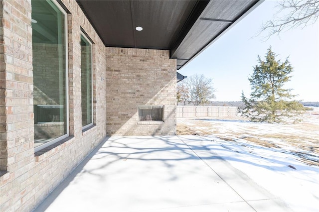 snow covered patio with an outdoor brick fireplace and fence