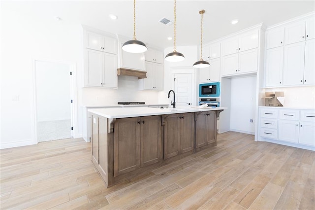 kitchen with oven, a kitchen island with sink, white cabinets, light countertops, and hanging light fixtures