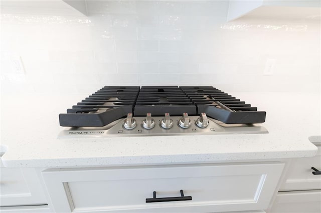 details with light stone countertops, tasteful backsplash, stainless steel gas stovetop, and white cabinets