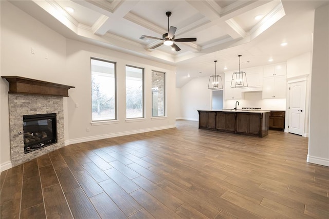 unfurnished living room featuring a ceiling fan, a stone fireplace, dark wood-style flooring, a sink, and baseboards
