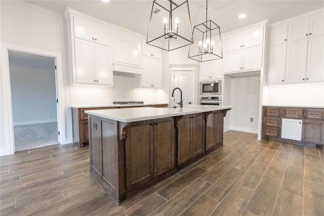 kitchen featuring white cabinetry, stainless steel oven, black microwave, pendant lighting, and a kitchen island with sink