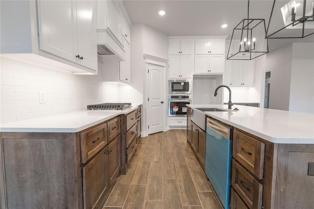 kitchen featuring hanging light fixtures, dark hardwood / wood-style floors, stainless steel appliances, a kitchen island with sink, and white cabinets