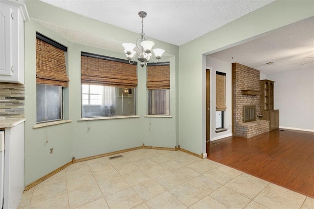 unfurnished dining area featuring a textured ceiling, light hardwood / wood-style floors, a brick fireplace, and a notable chandelier