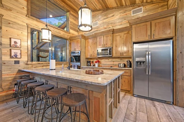 kitchen featuring wooden walls, hanging light fixtures, and stainless steel appliances