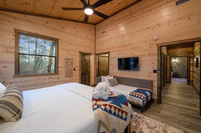 bedroom with ceiling fan, hardwood / wood-style floors, wood walls, and vaulted ceiling