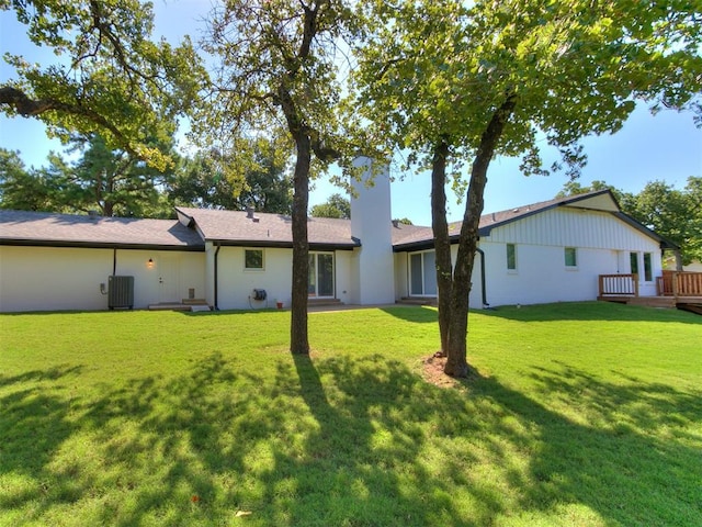 rear view of house with central AC unit and a lawn