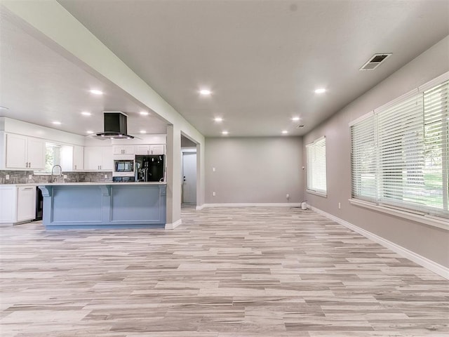 kitchen with a wealth of natural light, white cabinets, black appliances, and wall chimney range hood