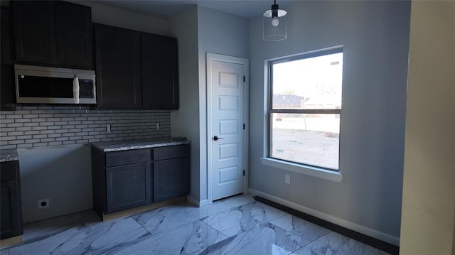 kitchen featuring hanging light fixtures, backsplash, light stone counters, and plenty of natural light