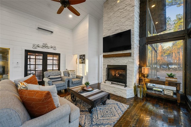 living room featuring a wall mounted AC, dark wood-type flooring, ceiling fan, high vaulted ceiling, and a stone fireplace